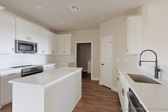 kitchen featuring appliances with stainless steel finishes, white cabinets, a kitchen island, sink, and dark hardwood / wood-style floors