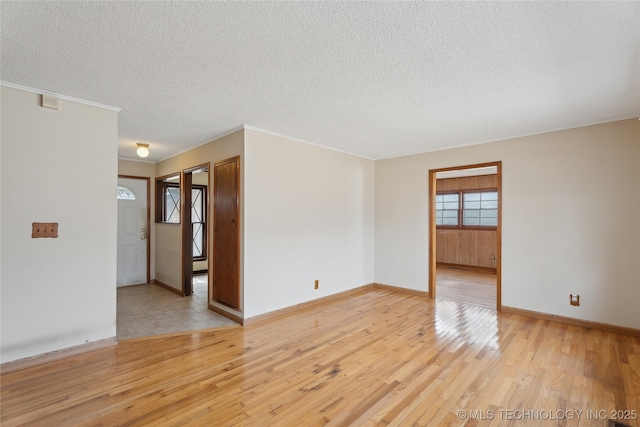 empty room featuring light wood-type flooring, a textured ceiling, and ornamental molding