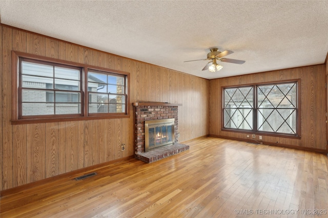 unfurnished living room with a fireplace, ceiling fan, light hardwood / wood-style floors, and a textured ceiling