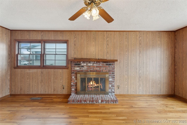 unfurnished living room featuring light hardwood / wood-style floors, ceiling fan, a textured ceiling, and a fireplace