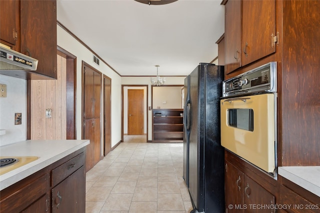 kitchen with black refrigerator, hanging light fixtures, wall oven, light tile patterned floors, and a chandelier