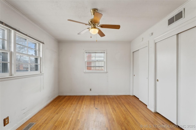 unfurnished bedroom with ornamental molding, light hardwood / wood-style flooring, ceiling fan, and multiple closets