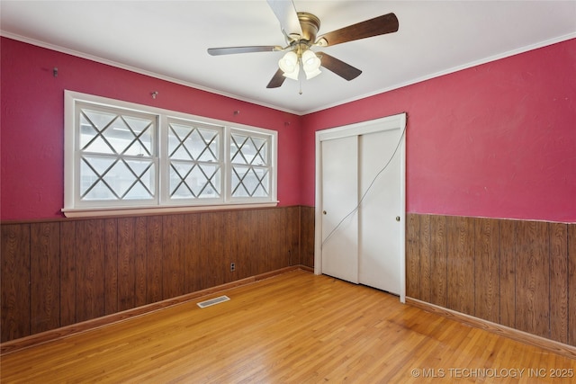 unfurnished bedroom featuring ceiling fan, a closet, wooden walls, and light hardwood / wood-style floors