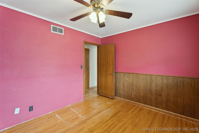 spare room featuring ceiling fan, ornamental molding, light hardwood / wood-style floors, and wood walls