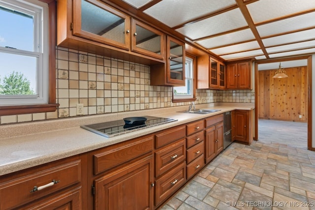 kitchen with wooden walls, black electric cooktop, decorative light fixtures, backsplash, and sink