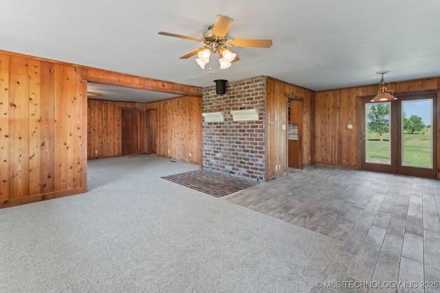 unfurnished living room featuring ceiling fan, carpet, and wood walls