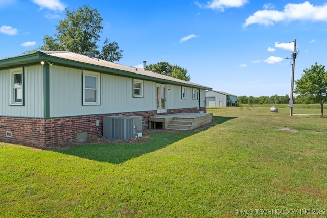 rear view of house featuring central AC unit and a lawn