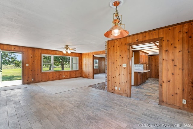 unfurnished living room featuring ceiling fan, wood walls, and light hardwood / wood-style floors