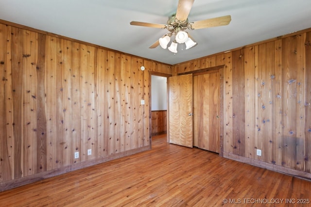 empty room featuring ceiling fan, wood walls, and hardwood / wood-style floors