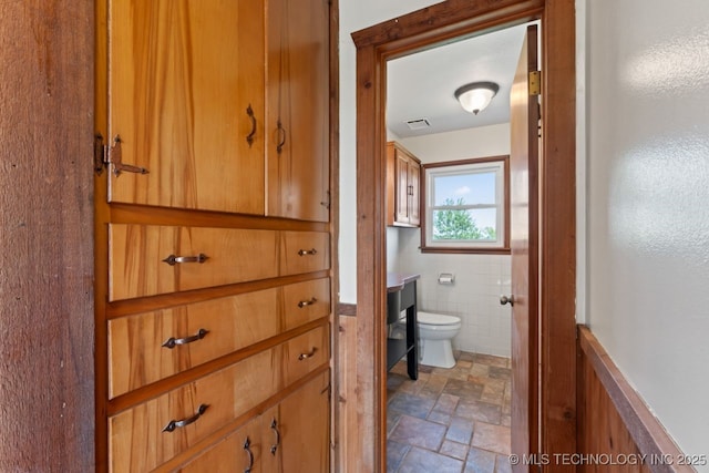 bathroom with toilet and tile walls