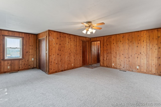 spare room with ceiling fan, crown molding, light colored carpet, and wooden walls