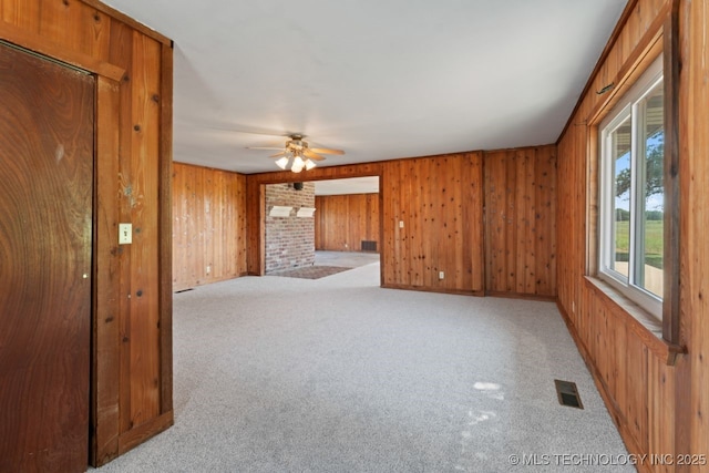 carpeted spare room with ceiling fan, wood walls, and a fireplace