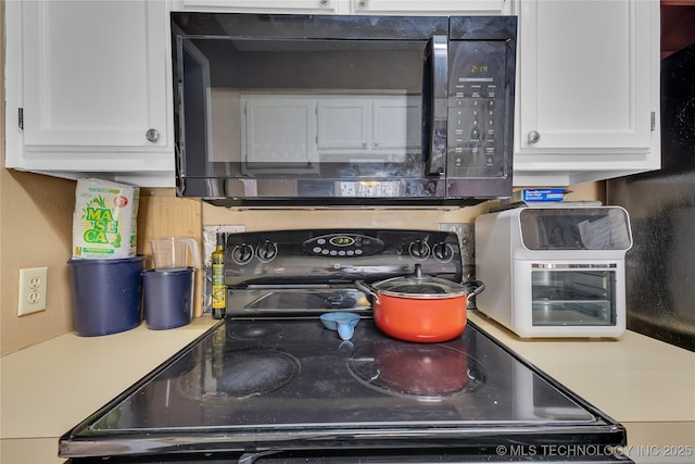 kitchen featuring black microwave, white cabinetry, light countertops, and electric stove