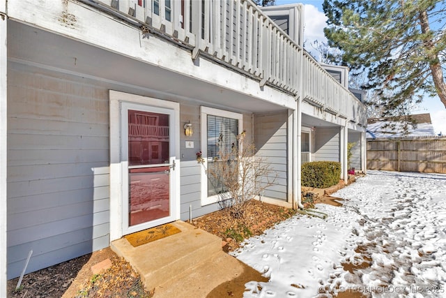 snow covered property entrance featuring a balcony and fence