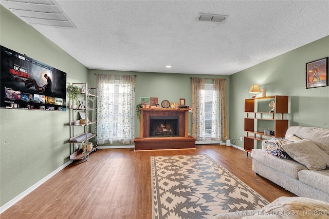 living area featuring a warm lit fireplace, visible vents, baseboards, and wood finished floors