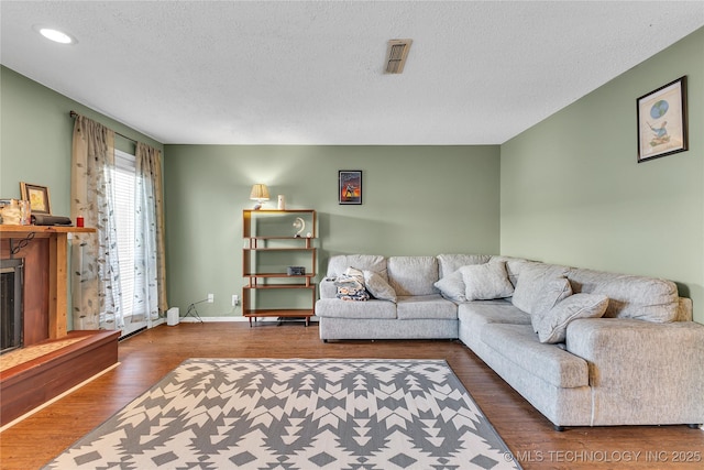 living area with visible vents, a fireplace with raised hearth, a textured ceiling, and wood finished floors