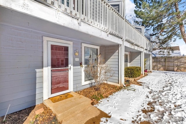 snow covered property entrance featuring fence and a balcony