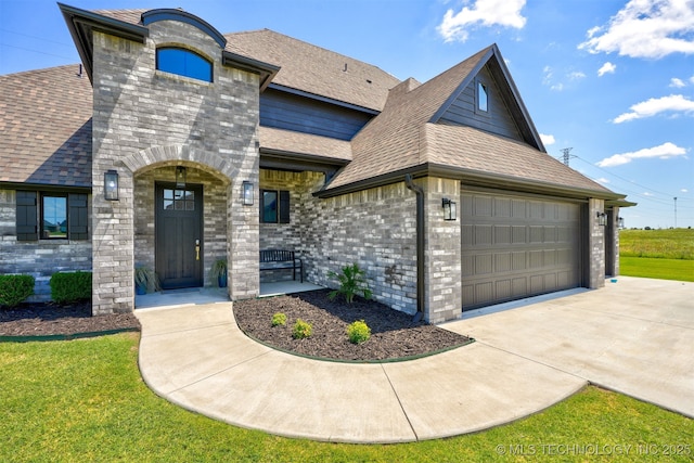 french country inspired facade with driveway, roof with shingles, an attached garage, a front lawn, and brick siding