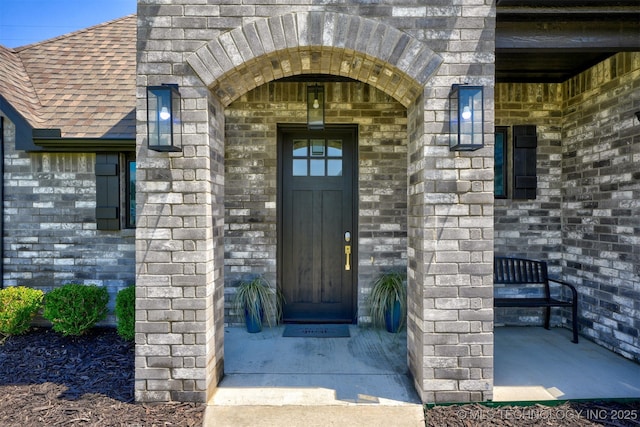 view of exterior entry featuring stone siding, a shingled roof, and brick siding