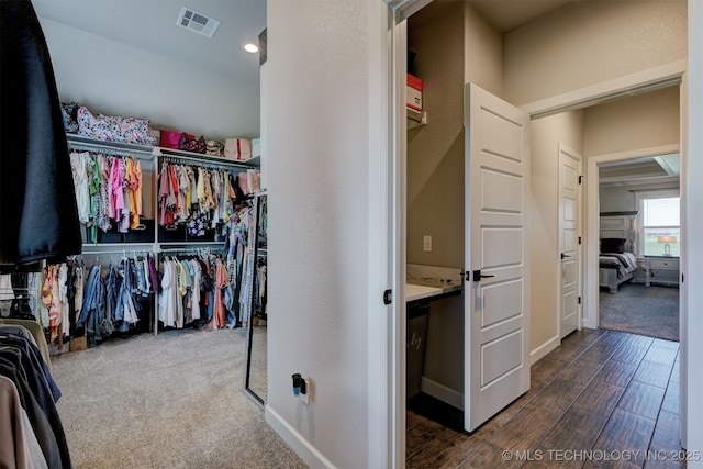 walk in closet with dark carpet, visible vents, and dark wood finished floors