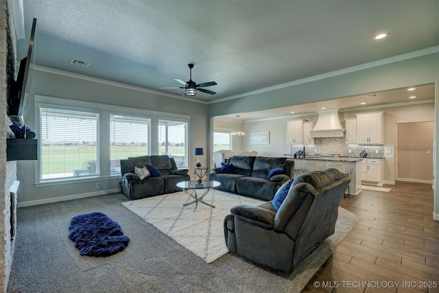 living room with ceiling fan, a textured ceiling, visible vents, baseboards, and crown molding