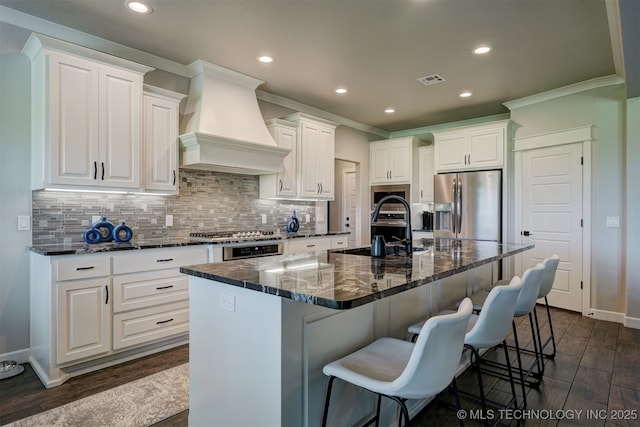 kitchen featuring white cabinets, stainless steel appliances, a large island with sink, and custom range hood