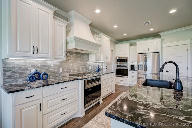 kitchen with decorative backsplash, custom range hood, appliances with stainless steel finishes, white cabinetry, and a sink