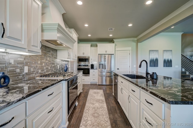 kitchen featuring appliances with stainless steel finishes, white cabinetry, a sink, dark stone countertops, and a large island with sink