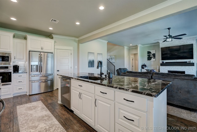 kitchen featuring white cabinets, an island with sink, appliances with stainless steel finishes, open floor plan, and a sink