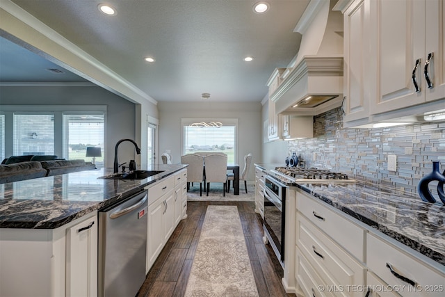 kitchen with white cabinets, dark wood finished floors, a sink, stainless steel appliances, and backsplash