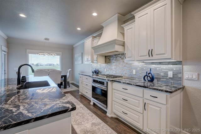 kitchen featuring a sink, white cabinets, appliances with stainless steel finishes, custom exhaust hood, and tasteful backsplash