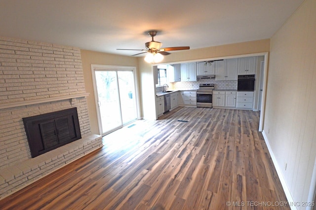 kitchen with dark wood-style floors, stainless steel appliances, gray cabinets, a sink, and under cabinet range hood