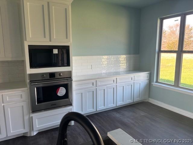 kitchen with black microwave, oven, white cabinets, light countertops, and backsplash