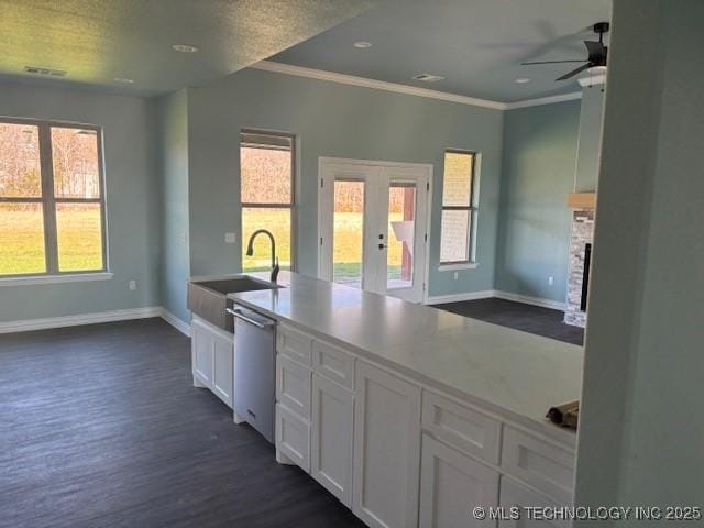 kitchen with french doors, a fireplace, stainless steel dishwasher, white cabinets, and a sink