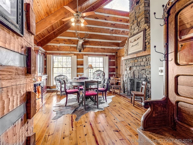 dining area featuring beam ceiling, light hardwood / wood-style flooring, a stone fireplace, high vaulted ceiling, and ceiling fan