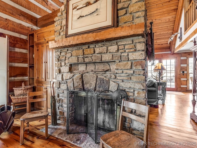 room details with hardwood / wood-style flooring, wooden walls, beamed ceiling, and a stone fireplace