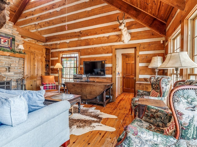 living room with a stone fireplace, wood walls, lofted ceiling with beams, and light hardwood / wood-style flooring