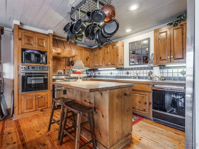 kitchen with a center island, butcher block countertops, black appliances, and decorative backsplash