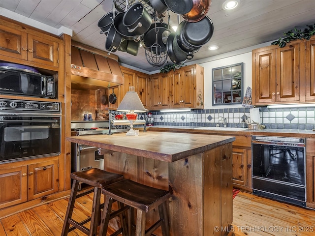 kitchen featuring black appliances, wood counters, a center island, custom exhaust hood, and a kitchen bar