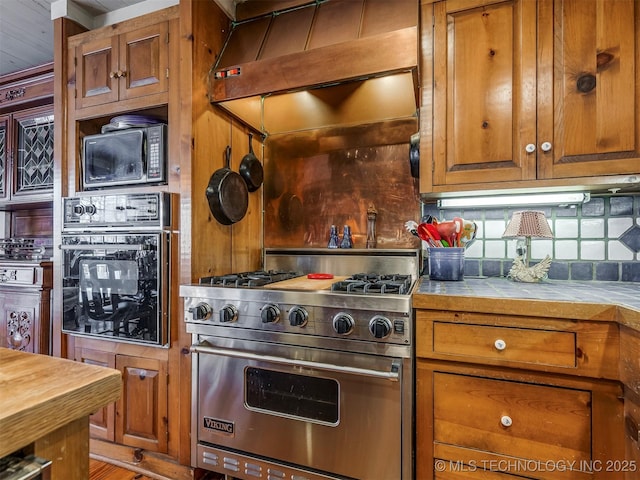 kitchen featuring tile counters, black appliances, tasteful backsplash, and wall chimney exhaust hood