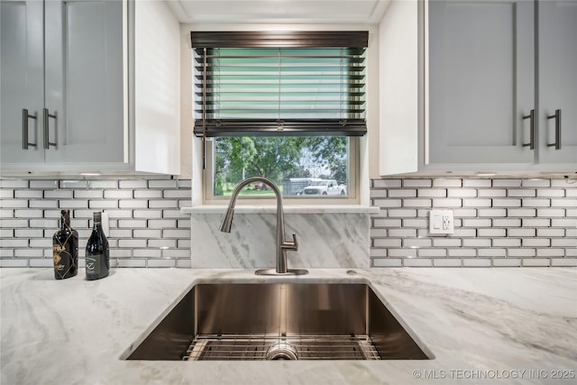 kitchen featuring decorative backsplash, light stone countertops, and sink