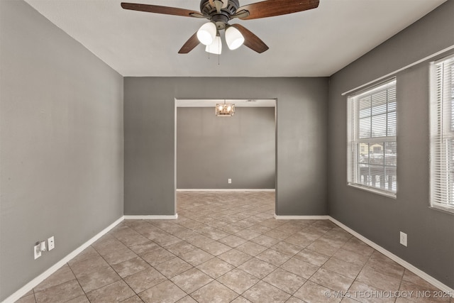 empty room featuring ceiling fan with notable chandelier, light tile patterned flooring, and baseboards