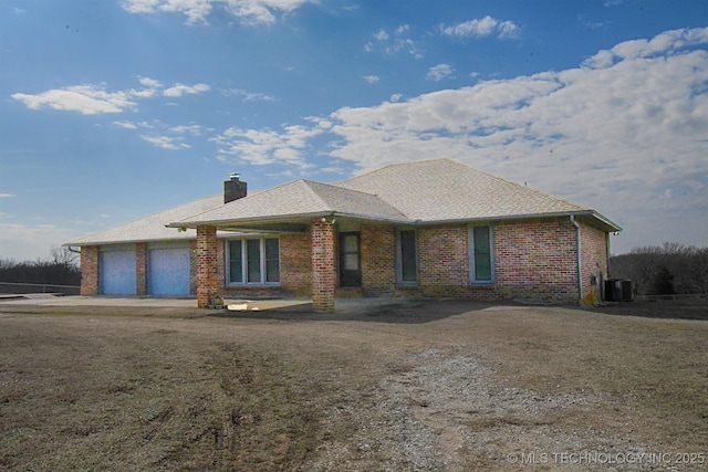 view of front of property featuring brick siding, an attached garage, central AC, and a chimney