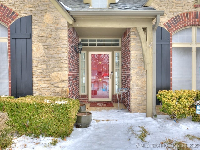 view of exterior entry featuring stone siding, a shingled roof, and brick siding