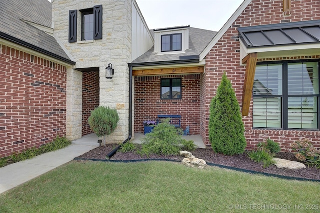 entrance to property featuring a lawn, stone siding, a shingled roof, and brick siding