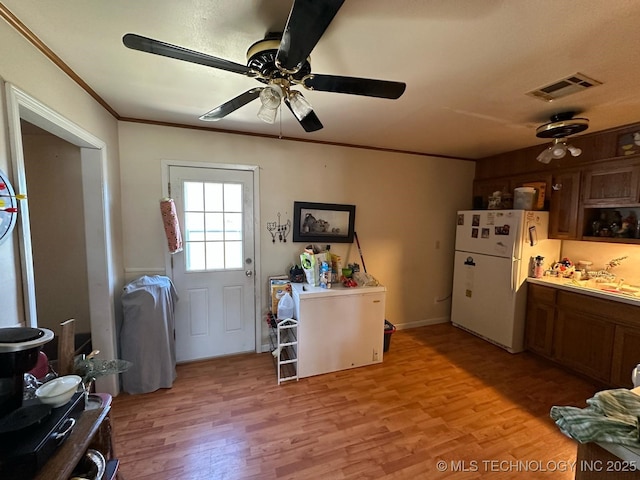 kitchen featuring light wood finished floors, visible vents, brown cabinetry, freestanding refrigerator, and crown molding