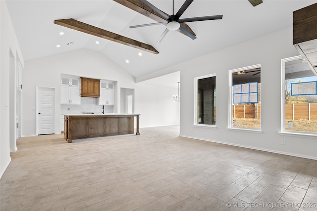 unfurnished living room featuring high vaulted ceiling, beam ceiling, a sink, and ceiling fan with notable chandelier