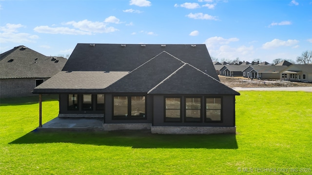 back of house featuring a patio, brick siding, roof with shingles, a lawn, and a residential view