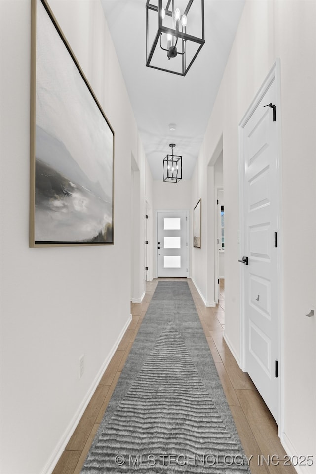 hall featuring wood finished floors, baseboards, and an inviting chandelier