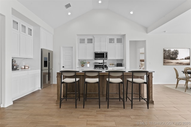 kitchen featuring light countertops, appliances with stainless steel finishes, glass insert cabinets, a kitchen island with sink, and white cabinetry